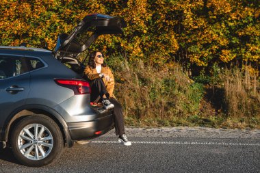 As she sits in trunk of her vehicle, woman enjoys sun as she enjoys the warmth