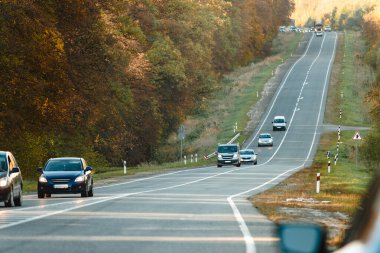 panorama of cars driving on the highway through the autumn forest