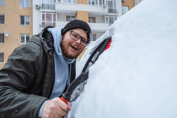 man cleans car from snow
