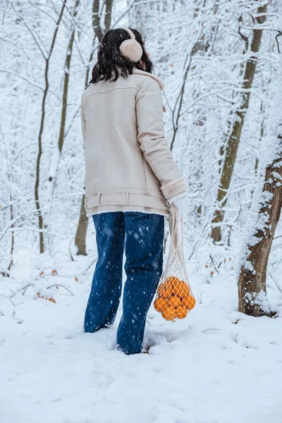 Woman walking with tangerines in wicker bag on snowy day