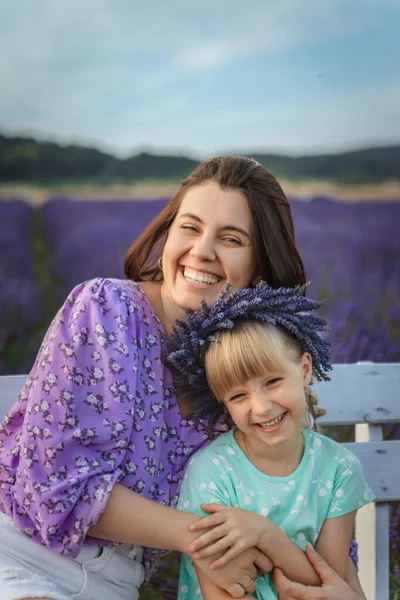 happy mother and daughter sitting on a bench at a lavender field