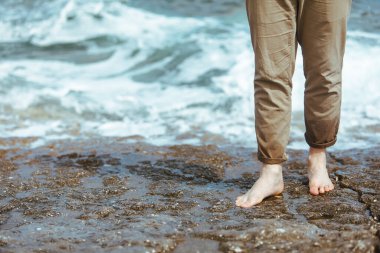 Deniz kıyısında yürürken pantolonlu ıslak adam bacakları suyun tadını çıkarıyor. yaz tatili