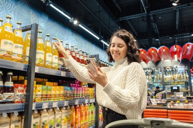 a woman buys juice from a grocery list on her phone in supermarket