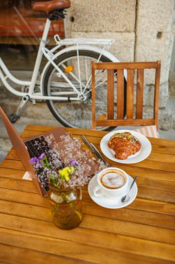 Bir dizüstü bilgisayar, kruvasan ve kafe yaz terasında kahve.