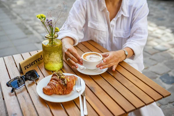 A woman has reserved a table for breakfast on the cafes summer terrace. a crispy croissant with coffee