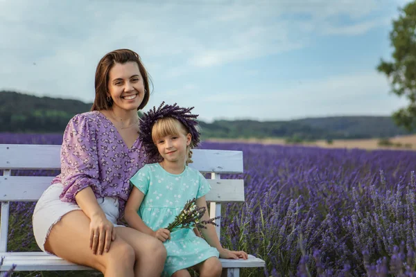happy mother and daughter sitting on a bench at a lavender field