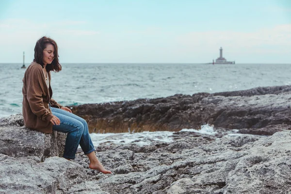Donna Seduta Sulla Spiaggia Rocciosa Del Mare Jeans Bagnati Faro — Foto Stock