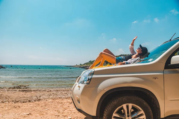 快乐的女人在海上夏季海滩坐在汽车引擎盖度假的概念 — 图库照片