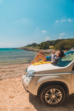 Deniz yaz plajında mutlu bir kadın araba kaputu tatilinde oturuyor.