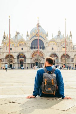 Yerde oturan genç adam Katedral Saint Marco Bazilika fotokopi alanına bakıyor. seyahat kavramı