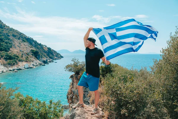ギリシャの旗を持った男が夏休みに崖の海で — ストック写真