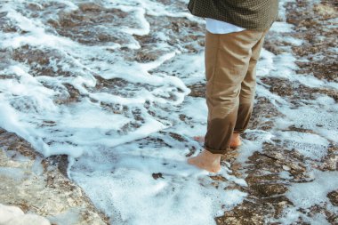 Deniz kıyısında yürürken pantolonlu ıslak adam bacakları suyun tadını çıkarıyor. yaz tatili