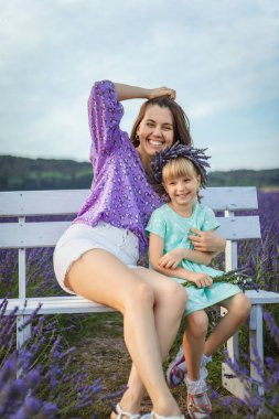 happy mother and daughter sitting on a bench at a lavender field