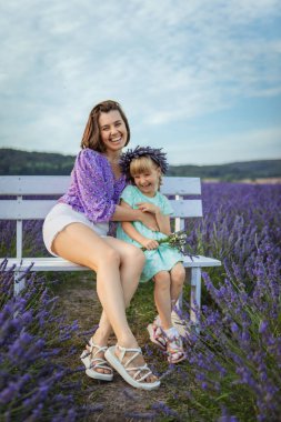 happy mother and daughter sitting on a bench at a lavender field