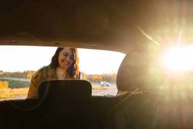 Gülümseyen kadın eşyaları arabanın bagajından çıkarır, içeriden bakar.