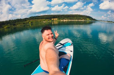 Mutlu adam gölün ortasında yemek masasında selfie çekiyor.