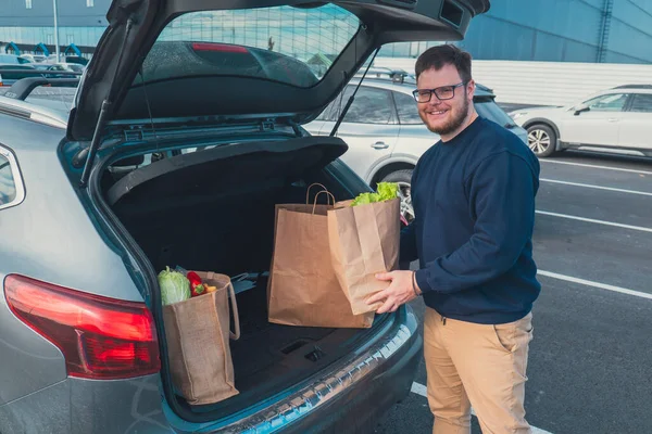 happy man put groceries bag in car trunk mall parking place