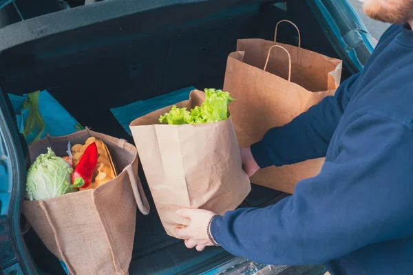 man hands with groceries bags put it in car trunk close up