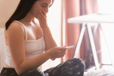 Yatakta pozitif hamilelik testi olan endişeli bir kadın.