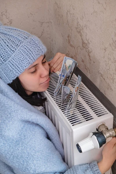 A woman hugs a radiator and looks at the money she will pay for heat