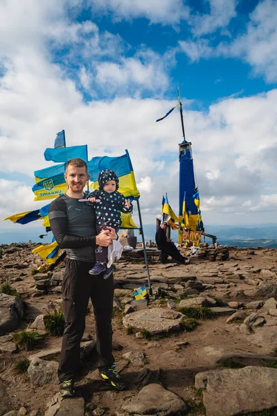 Man with Baby on Mountain near Ukrainian Flags