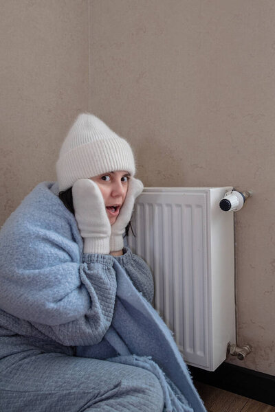 тепло одетый женщина сидит рядом с радиатором и шокирован отсутствием отопления