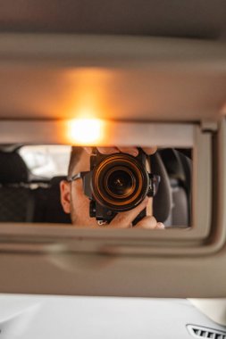 Adam aynada, arabada kamerayla fotoğraf çeker.