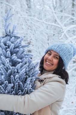 Çekici bir kadının ellerinde, karla kaplı Noel ağacı tutuluyor.