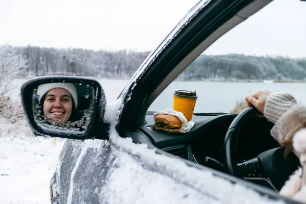 woman in car eating burger and drink coffee at frozen lake beach
