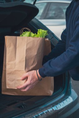 Market poşeti taşıyan adam ellerini arabanın bagajına koy.