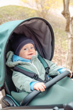 Bahar parkında bebek arabasında gülümseyen bebek.