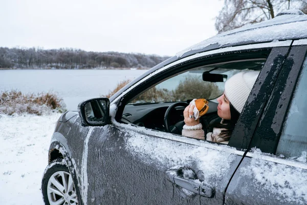 woman eat burger sitting in car at the frozen lake beach copy space