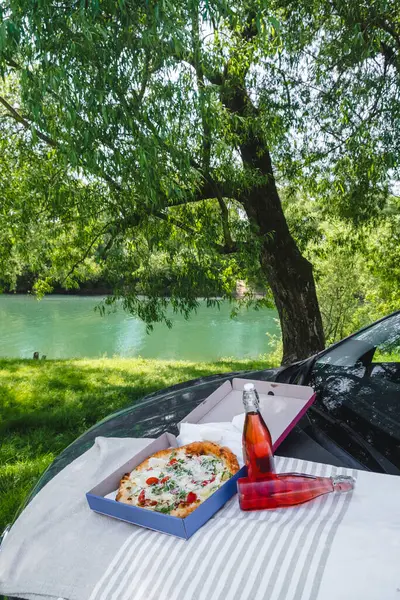 outdoors picnic pizza with drink on car hood at the river side summer time