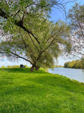 Yeşil çimleri, ağaçları ve nehri olan bir manzara.