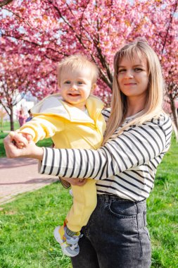 Mutlu anne sakura ağacının altında bebeği kollarında tutuyor.