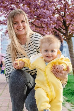 Çocuk annesiyle birlikte kiraz ağaçlarının arasında yürümeyi öğreniyor..