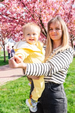 Neşeli anne ve bebek çiçek açan sakura ağacının yanında.