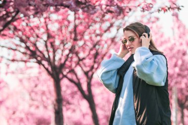 Güneş gözlüklü kadın portresi. Kulaklıklı. Arka plan fotokopi alanında sakura çiçeği açıyor.