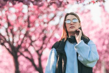 Güneş gözlüklü kadın portresi. Kulaklıklı. Arka plan fotokopi alanında sakura çiçeği açıyor.