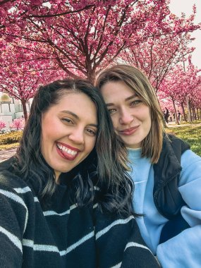 İki mutlu kız arkadaş bahar zamanı çiçek açan Sakura ağacının altında selfie çekiyorlar.