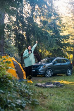 Arka planda Serene Forest SUV 'de sabah kahvesi içen mutlu bir kadın.