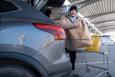 Gülümseyen Adam erzakları araba bagajına yüklüyor.