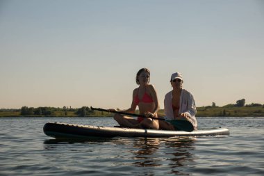 Women Enjoying Paddleboarding on a Sunny Day summertime clipart