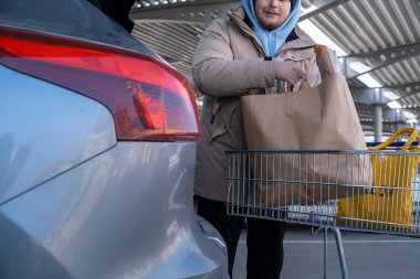 Gülümseyen Adam erzakları araba bagajına yüklüyor.