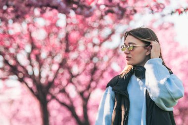 Güneş gözlüklü kadın portresi. Kulaklıklı. Arka plan fotokopi alanında sakura çiçeği açıyor.