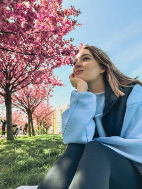 Çiçek açan sakura ağaçlarının önünde poz veren güzel bir kadın.