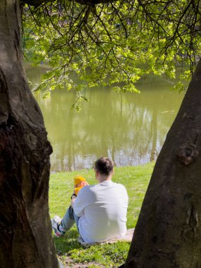 Baba ve yeni doğan oğlu güneşli bahar günü göl kenarında dinleniyorlar.