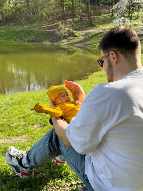 Baba ve yeni doğan oğlu güneşli bahar günü göl kenarında dinleniyorlar.