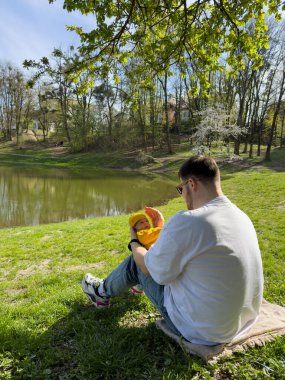 Baba ve yeni doğan oğlu güneşli bahar günü göl kenarında dinleniyorlar.