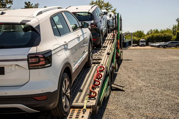 New white crossover - SUV on car carrier trailer, car-carrying trailer, car hauler, auto transport trailer, semi-trailer. Rear view car. Rear view trailer. Visible taillamps.